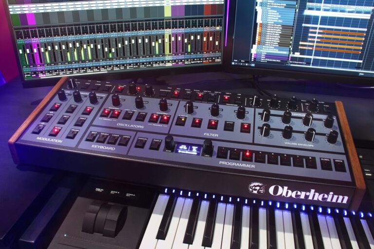 The Oberheim OB-X8 Desktop Module in a studio environment with a controller keyboard and monitor screens showing DAW tracks.